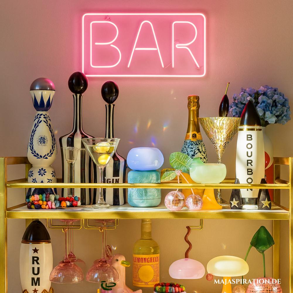 Home Bar mit rosa Leuchtschrift auf goldenem Küchenwagen