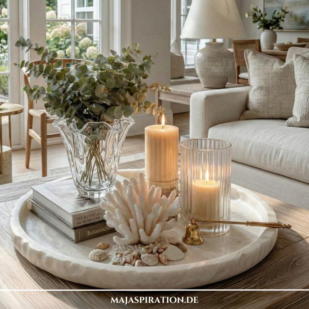 Strukturiertes weißes Tablett mit großer Koralle, Eukalyptus in Glasvase und Kerzen als maritime Tablett-Deko auf einem hölzernen Couchtisch.
