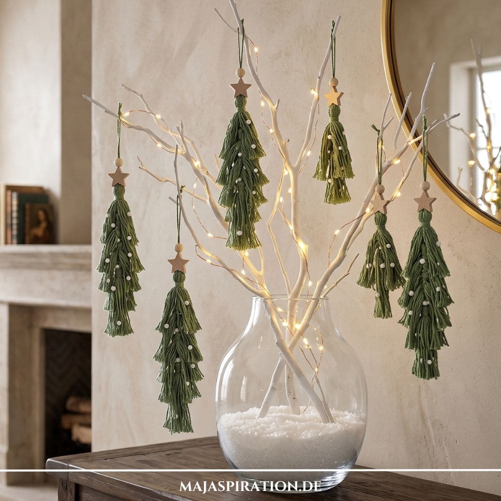 Nat&uuml;rliche DIY Weihnachtsdeko: Selbstgemachte gr&uuml;ne Makramee-Tannenb&auml;ume mit Holzsternen und Perlen h&auml;ngen an beleuchteten &Auml;sten in einer Glasvase.
